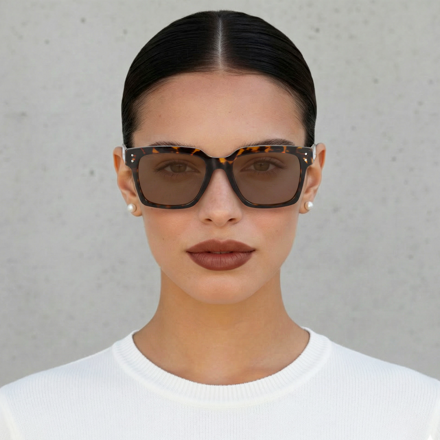 Woman wearing tortoiseshell sunglasses with a plain background