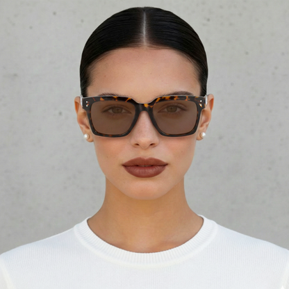 Woman wearing tortoiseshell sunglasses with a plain background