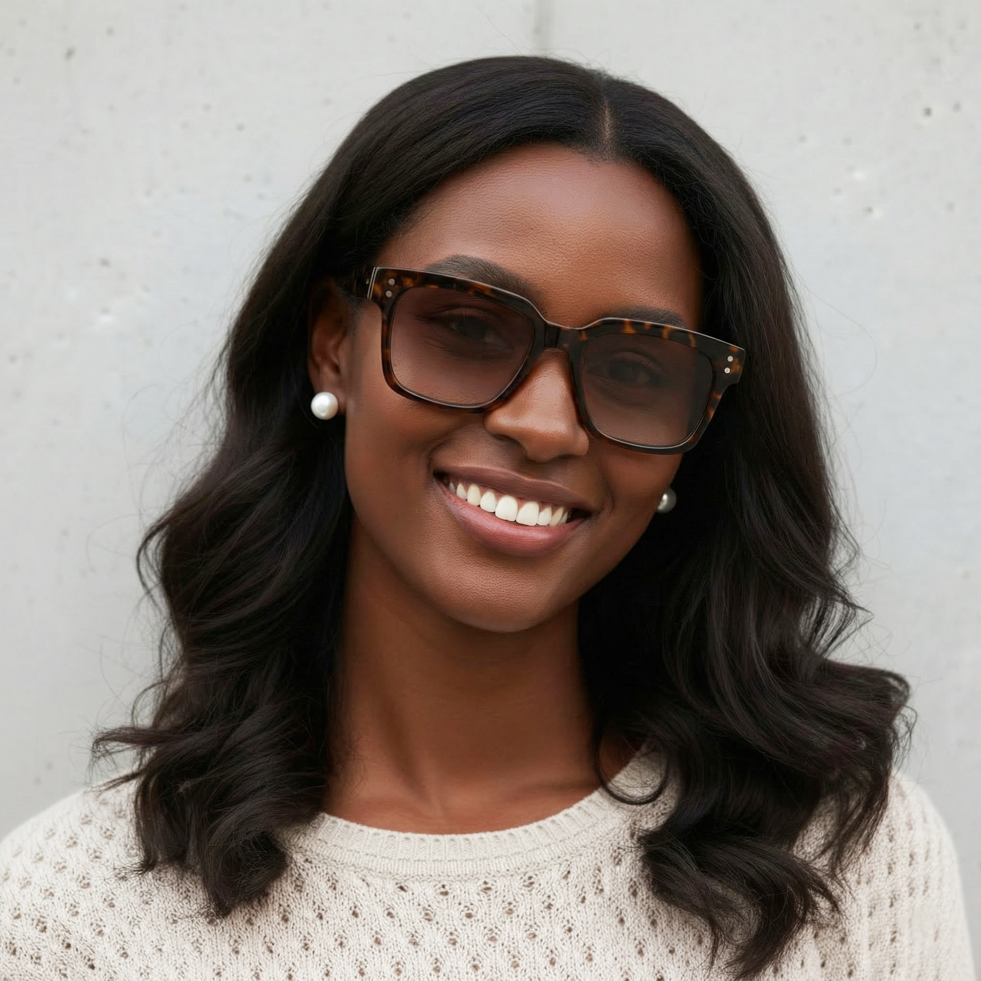 Woman wearing sunglasses and a white sweater against a gray background